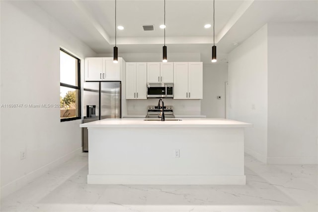 kitchen featuring a center island with sink, white cabinets, hanging light fixtures, a tray ceiling, and stainless steel appliances