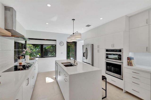 kitchen with pendant lighting, wall chimney range hood, sink, an island with sink, and appliances with stainless steel finishes