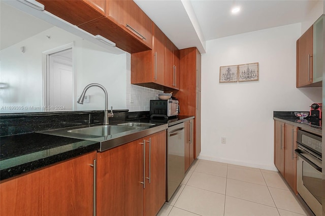 kitchen with sink, decorative backsplash, dark stone countertops, light tile patterned floors, and stainless steel appliances