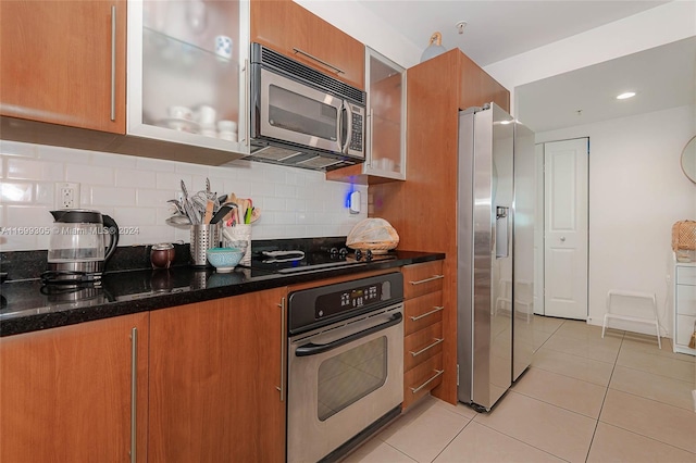 kitchen featuring backsplash, light tile patterned floors, stainless steel appliances, and dark stone counters