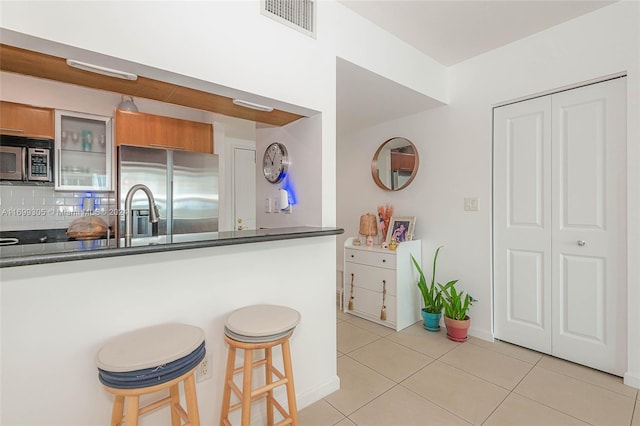 kitchen featuring backsplash, a breakfast bar, light tile patterned floors, and stainless steel appliances