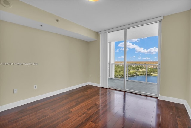 unfurnished room featuring dark hardwood / wood-style floors, a water view, and a wall of windows