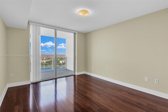 unfurnished room with a water view, dark wood-type flooring, and a wall of windows