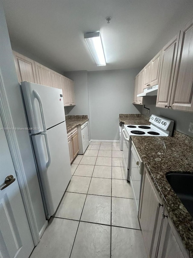 kitchen featuring dark stone countertops, light brown cabinets, light tile patterned flooring, and white appliances