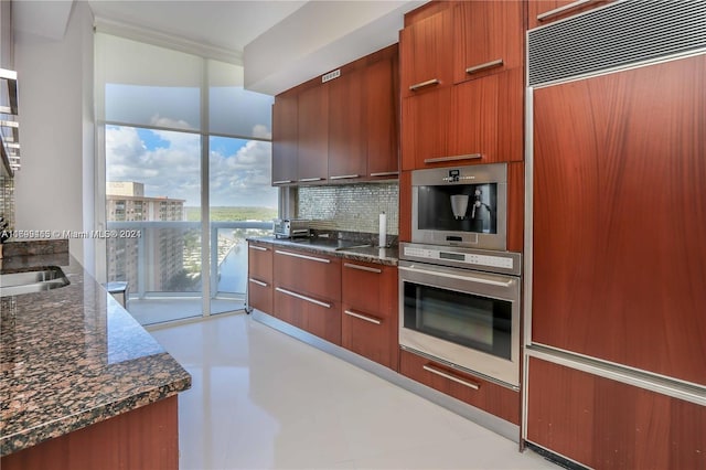 kitchen with paneled fridge, stainless steel oven, backsplash, and dark stone counters