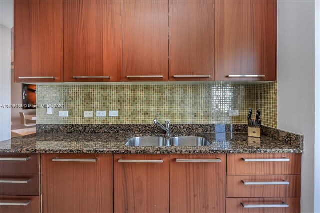 kitchen with backsplash, dark stone countertops, and sink