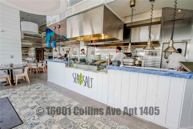 kitchen featuring white cabinets, pendant lighting, wooden walls, and exhaust hood