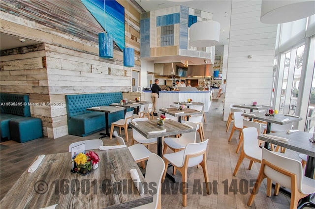 dining area featuring wood-type flooring, a towering ceiling, and wooden walls