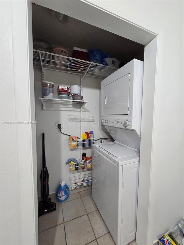 clothes washing area featuring light tile patterned floors and stacked washing maching and dryer