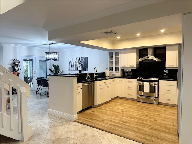 kitchen featuring white cabinetry, wall chimney range hood, crown molding, appliances with stainless steel finishes, and light wood-type flooring