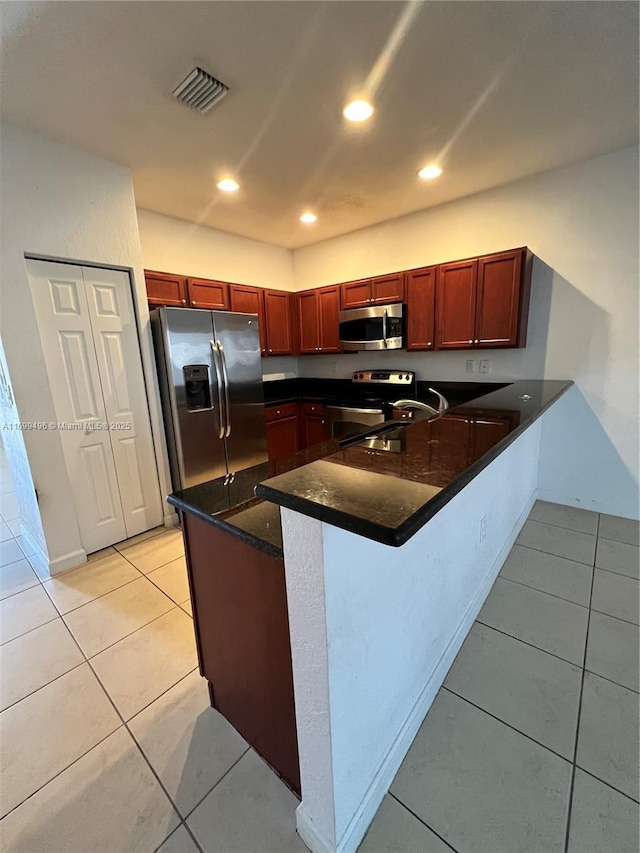 kitchen with sink, dark stone counters, light tile patterned floors, kitchen peninsula, and stainless steel appliances