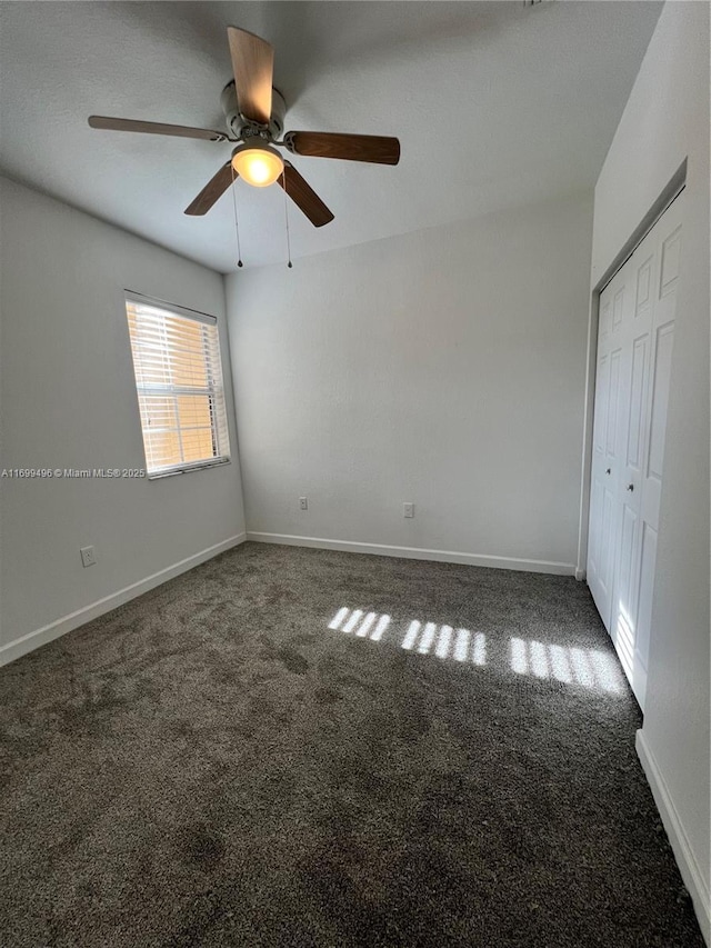 unfurnished bedroom featuring ceiling fan, dark carpet, and a closet