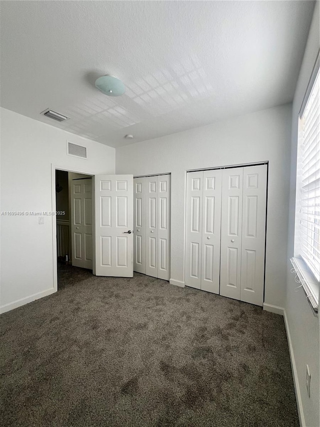 unfurnished bedroom with a textured ceiling, multiple closets, and dark colored carpet