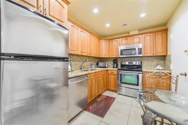 kitchen featuring sink, stainless steel appliances, light stone counters, backsplash, and light tile patterned floors