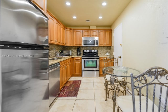 kitchen featuring light stone countertops, sink, backsplash, light tile patterned floors, and appliances with stainless steel finishes