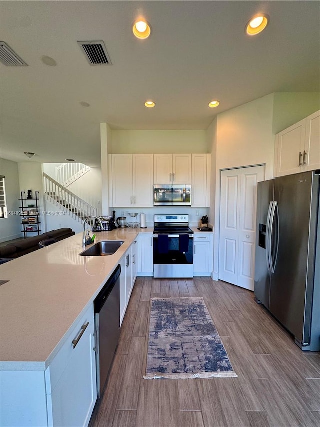 kitchen with sink, kitchen peninsula, wood-type flooring, white cabinets, and appliances with stainless steel finishes