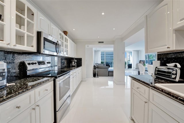 kitchen featuring appliances with stainless steel finishes, tasteful backsplash, dark stone counters, light tile patterned floors, and white cabinets