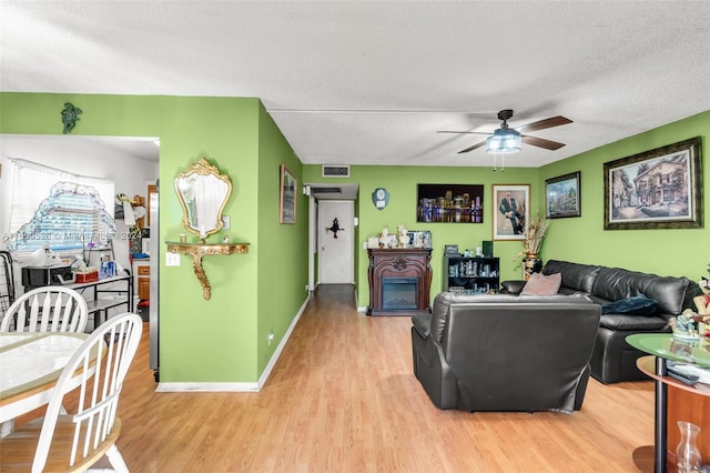 living room with ceiling fan, light hardwood / wood-style floors, and a textured ceiling