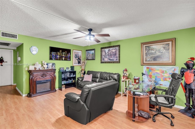 living room featuring ceiling fan, light hardwood / wood-style flooring, and a textured ceiling