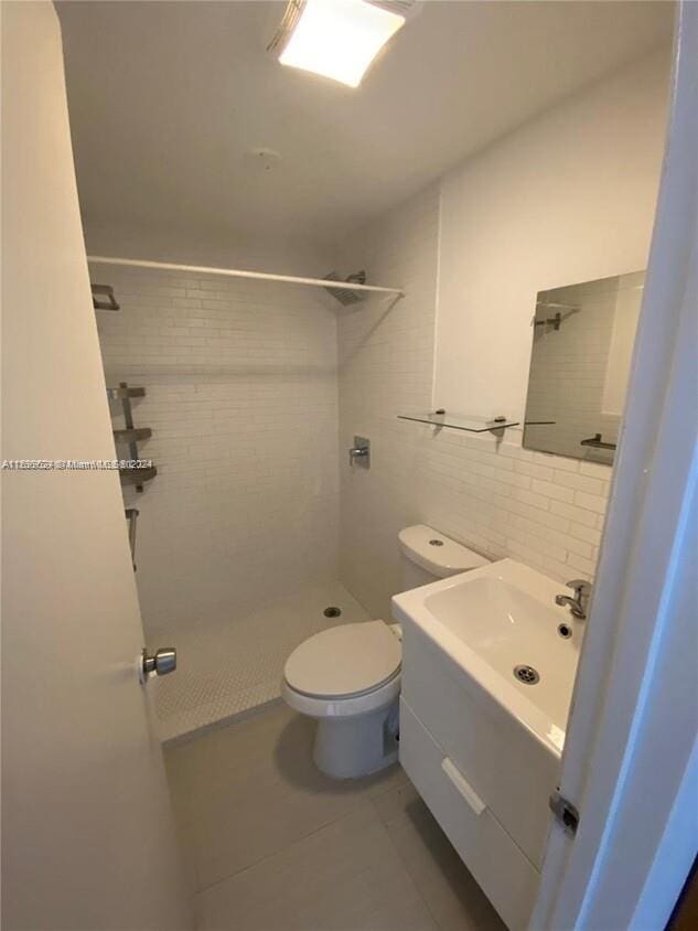 bathroom with vanity, tile patterned floors, toilet, tile walls, and a tile shower