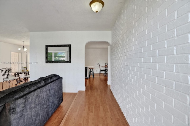 corridor featuring a textured ceiling, hardwood / wood-style flooring, an inviting chandelier, and brick wall