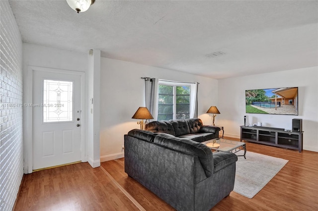 living room featuring hardwood / wood-style floors, a textured ceiling, and brick wall