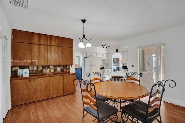 dining area with a textured ceiling, light wood-type flooring, and a notable chandelier