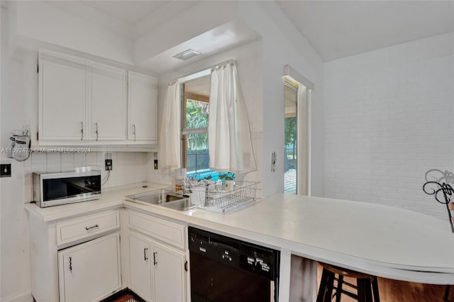 kitchen with white cabinetry, sink, black dishwasher, kitchen peninsula, and a breakfast bar area