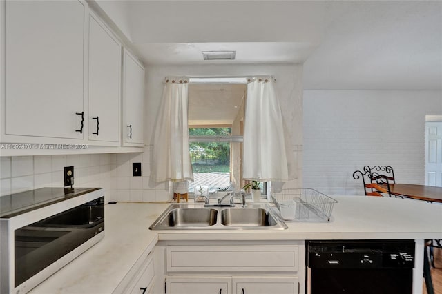 kitchen with kitchen peninsula, tasteful backsplash, sink, black dishwasher, and white cabinetry