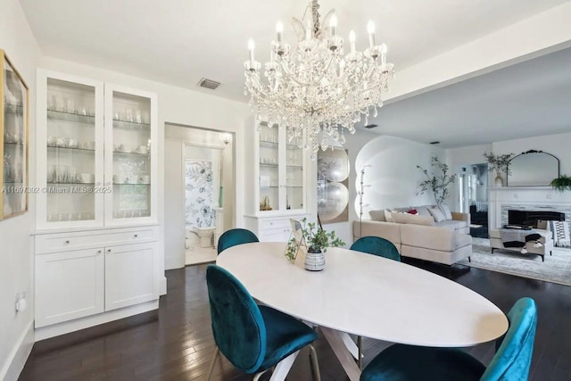 dining area featuring dark hardwood / wood-style floors, an inviting chandelier, and a fireplace