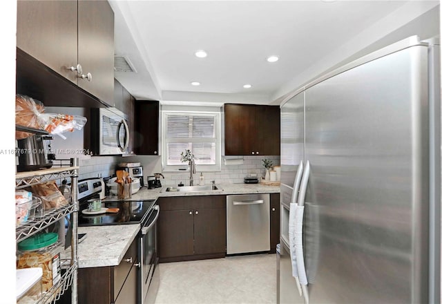 kitchen featuring light stone countertops, decorative backsplash, dark brown cabinets, stainless steel appliances, and sink