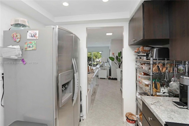 kitchen featuring stainless steel fridge with ice dispenser, dark brown cabinets, light tile patterned floors, and light stone counters