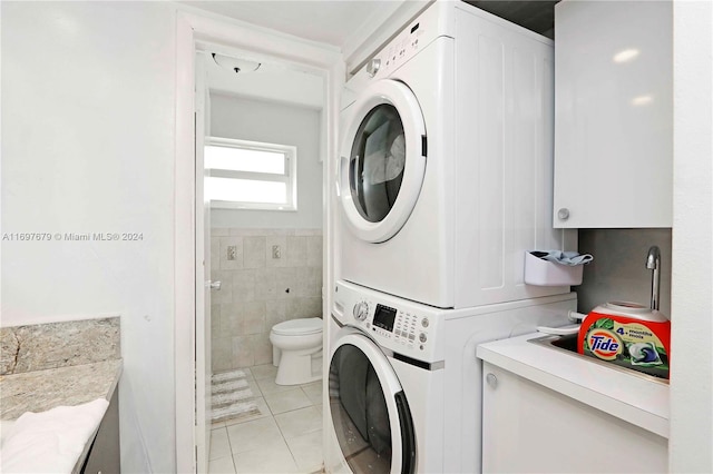 clothes washing area featuring stacked washer / dryer, light tile patterned flooring, and tile walls