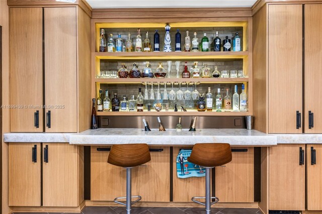 bar with dark tile patterned flooring and light brown cabinetry