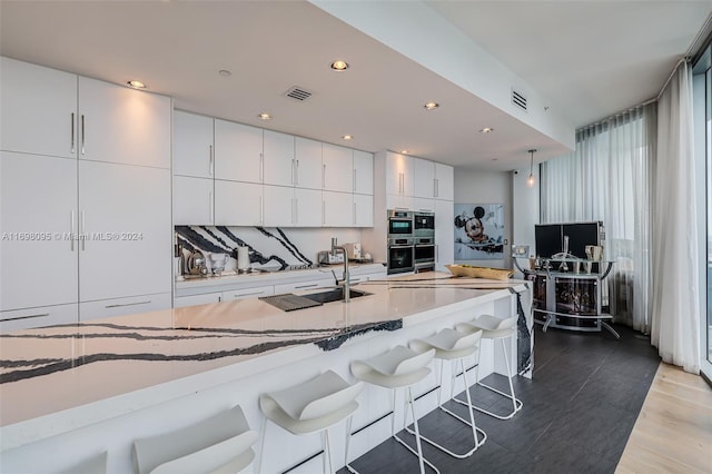 kitchen featuring white cabinets, hanging light fixtures, tasteful backsplash, a kitchen bar, and wood-type flooring