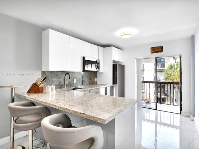 kitchen with a kitchen breakfast bar, stainless steel appliances, sink, white cabinetry, and kitchen peninsula