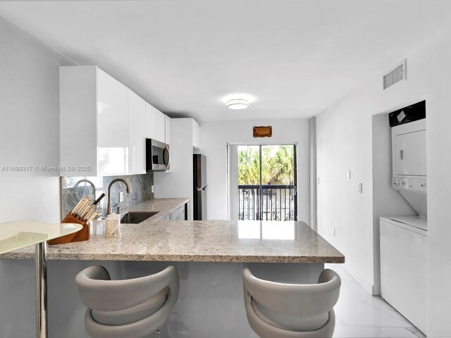 5390 W 21st Ct Unit 312, Hialeah, FL 33016 - kitchen featuring stainless steel microwave, a sink, stacked washing machine and dryer, light stone counters, and a peninsula