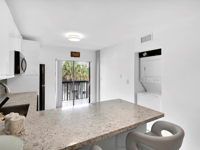 kitchen with white cabinetry, kitchen peninsula, a breakfast bar, sink, and stacked washer and clothes dryer