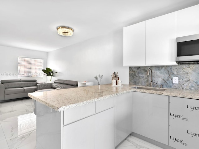 kitchen with sink, backsplash, light stone counters, kitchen peninsula, and white cabinets