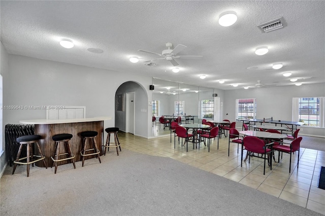 dining space with ceiling fan, light colored carpet, and a textured ceiling