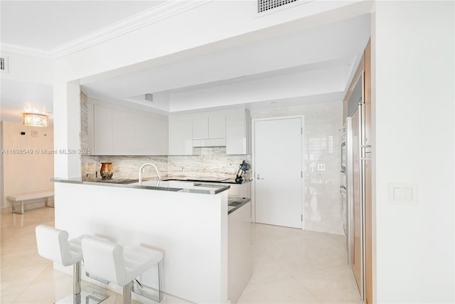 kitchen featuring dark countertops, visible vents, ornamental molding, white cabinets, and a peninsula