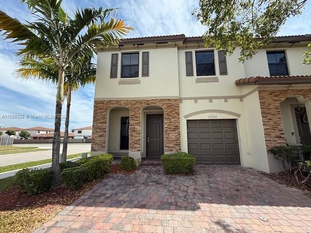 view of front facade featuring stucco siding, a tile roof, decorative driveway, stone siding, and an attached garage