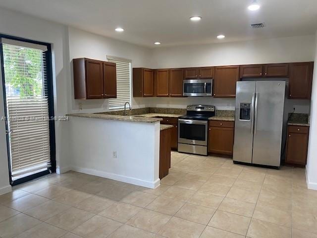 kitchen with kitchen peninsula, light stone countertops, stainless steel appliances, sink, and light tile patterned floors