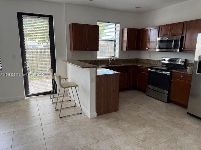 kitchen featuring a sink, a kitchen breakfast bar, dark countertops, appliances with stainless steel finishes, and a peninsula