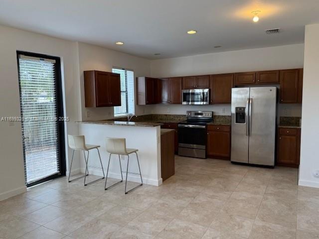 kitchen featuring baseboards, visible vents, a peninsula, stainless steel appliances, and dark countertops