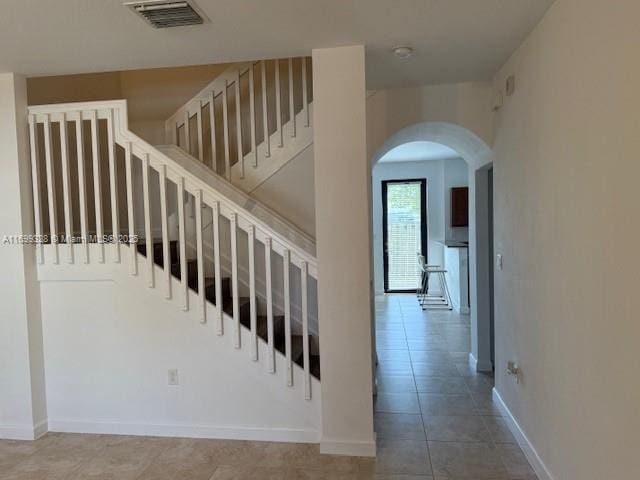 staircase with arched walkways, visible vents, tile patterned flooring, and baseboards