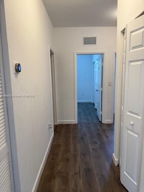 hallway featuring dark wood-style floors, visible vents, and baseboards