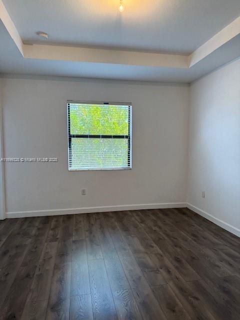 spare room featuring a tray ceiling, dark wood-style floors, and baseboards