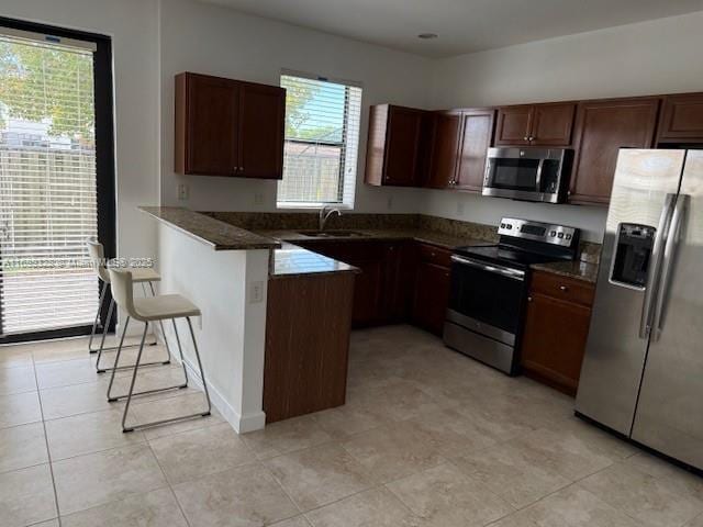 kitchen featuring dark countertops, a breakfast bar, a peninsula, stainless steel appliances, and a sink