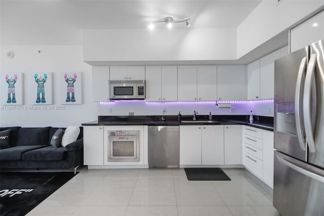 kitchen with white cabinets, dark countertops, open floor plan, stainless steel appliances, and a sink